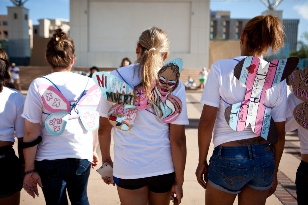 Feminine people standing next to each other, all wearing white, pink and blue butterfly wings.